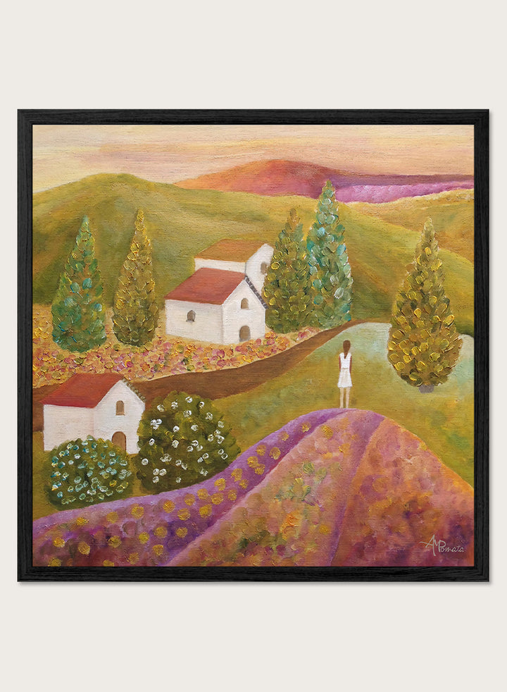 A framed landscape painting featuring rolling green hills, white houses with red roofs, tall conical trees, and a figure standing on a purple field. Shop Woman in Lavender Fields by Angeles M. Pomata, a colorful landscape and figurative art print featuring lavender fields, white houses, cypress trees, and rolling hills.