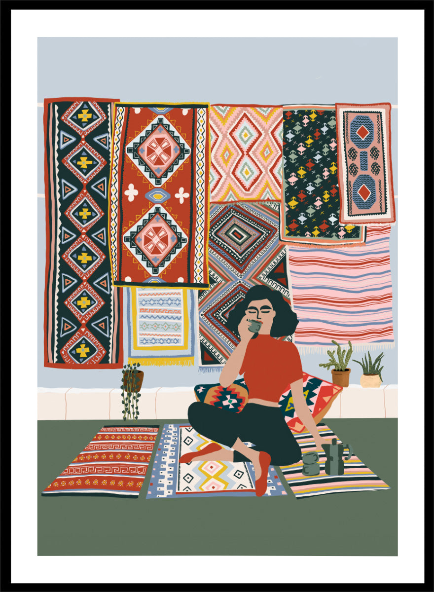 A framed art print featuring a stylized illustration of a woman sitting cross-legged on a patterned rug, surrounded by colorful geometric textiles hanging on a wall. Bohemian Coffee Morning by Ceyda Alasar interior art print featuring patterned rugs, floor cushions, potted plants, coffee, and colorful collected decor.