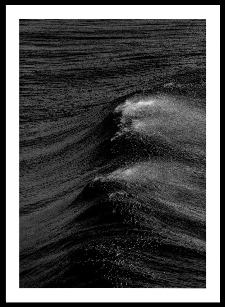 Black and white fine art photographic print of ocean waves, featuring a dramatic wave crest with white foam against dark textured water. Night Wave Cascade by Shot by Clint black-and-white ocean photography print featuring dark rolling waves, sea spray, and dramatic natural movement.