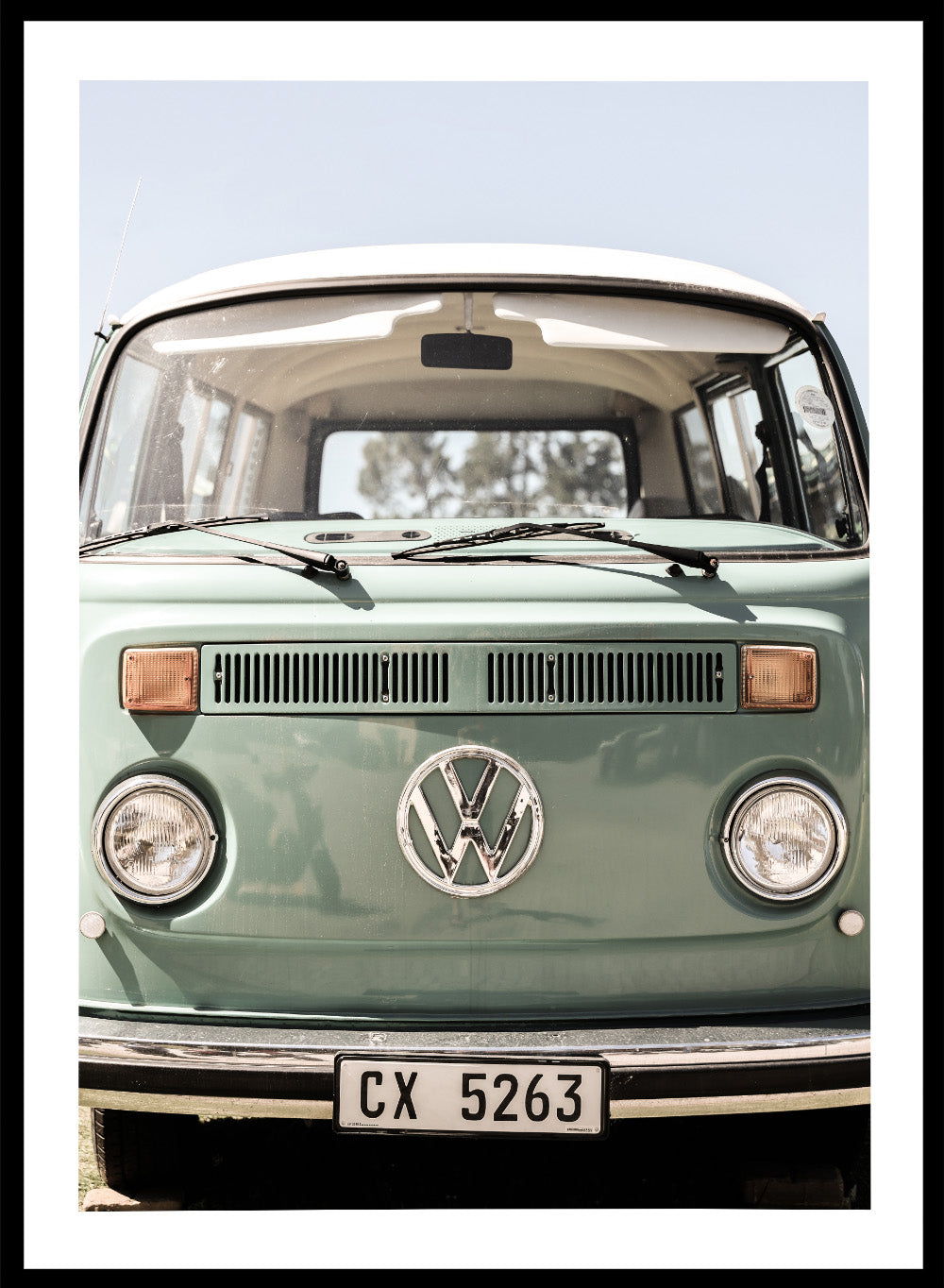 Front view of a vintage green Volkswagen van with clear sky background. Classic Design In Soft Green Tones by Shot by Clint car art print featuring a vintage Volkswagen camper van in soft sage green and warm sunlight.