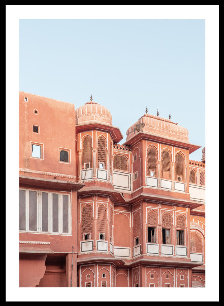 A framed art print featuring a photograph of the iconic pink sandstone Rajasthani palace, Udaipur, with white architectural details under a clear light blue sky. Terracotta Splendor by Shot by Clint architectural photography print featuring ornate palace windows, domed balconies, carved details, and warm coral tones.