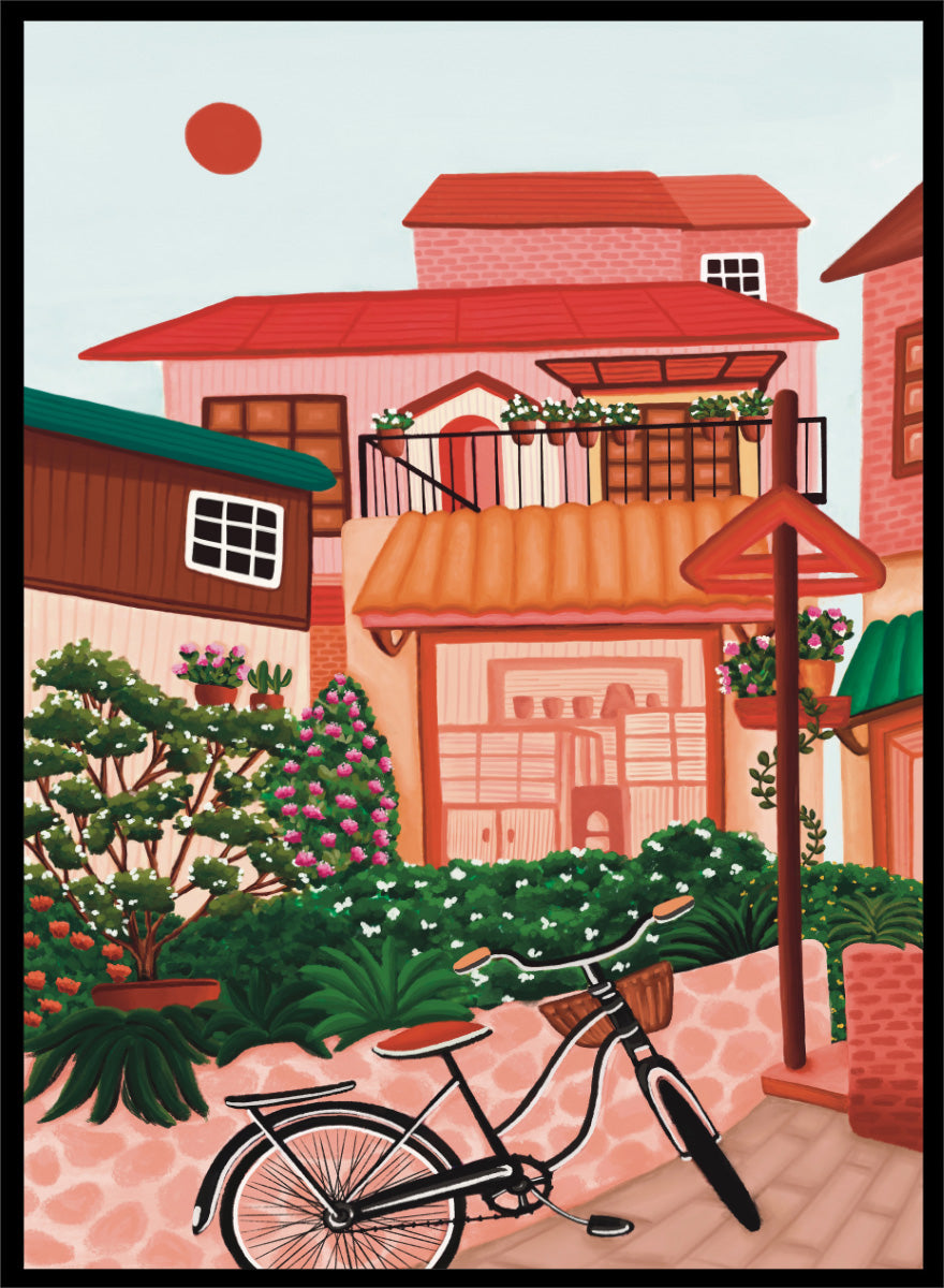 A colorful illustrated street scene with pink and peach buildings, green plants, flowers, a bicycle in the foreground, and a pale sky with a red sun. Shop Charming Village Street by Nidhi Kachhadiya, a colorful village wall art print featuring a bicycle, flower-filled homes, terracotta roofs, and warm pink and green tones.
