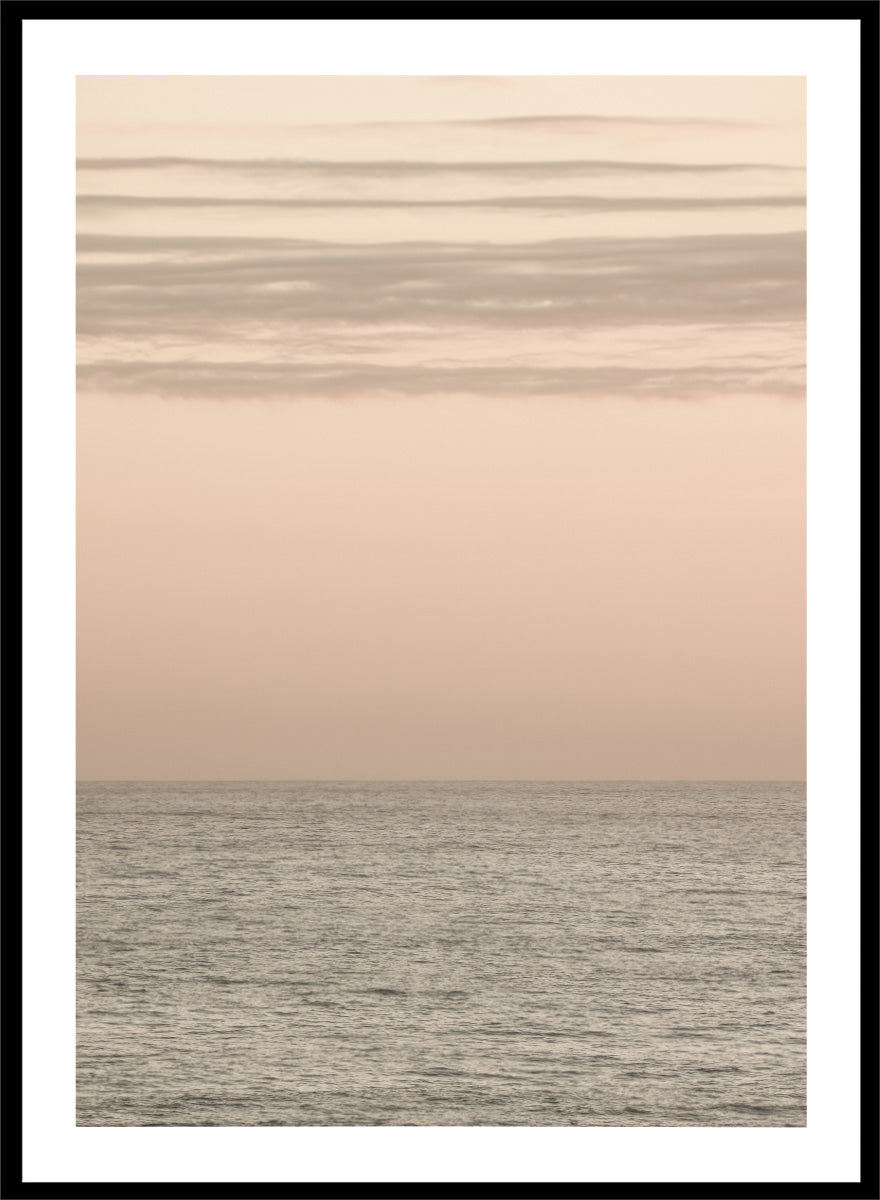 A minimalist framed art print depicting a calm seascape at dusk or dawn, with a soft peach and beige sky meeting a muted gray-blue ocean horizon. Serene Horizons by Shot by Clint features a soft peach sky and calm ocean horizon in a minimal coastal photograph with airy neutral tones.