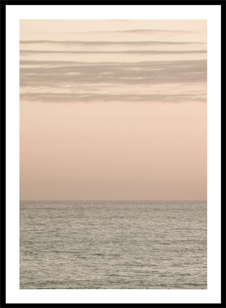 A minimalist framed art print depicting a calm seascape at dusk or dawn, with a soft peach and beige sky meeting a muted gray-blue ocean horizon. Serene Horizons by Shot by Clint features a soft peach sky and calm ocean horizon in a minimal coastal photograph with airy neutral tones.