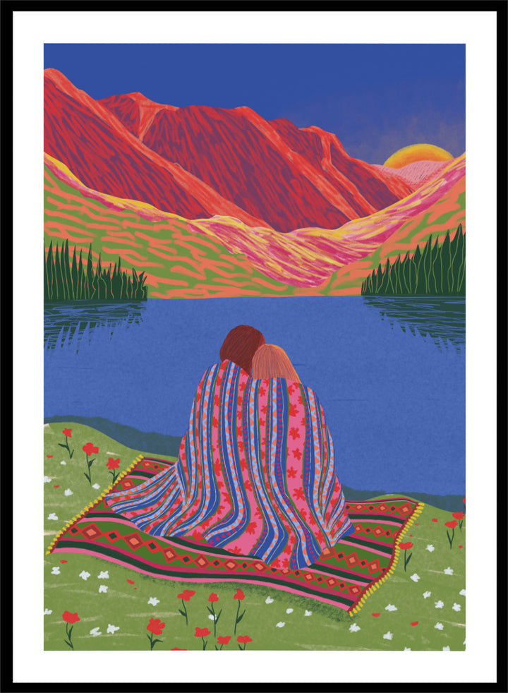 A framed art print featuring a stylized landscape illustration of two people sitting together on a patterned blanket by a blue lake, with red mountains and a yellow sun in the background. Cozy Lake Sunset art print by Ceyda Alasar features a lakeside embrace, vivid mountains, and a glowing sunset in rich, story-filled color.