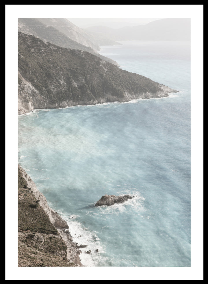 A framed photographic art print depicting a coastal landscape with a steep rocky cliff overlooking a calm, pale blue sea with a small rock formation in the foreground. Coastal Serenity by Shot by Clint coastal photography print featuring pale blue water, rugged cliffs, rocky shores, and a soft hazy horizon.