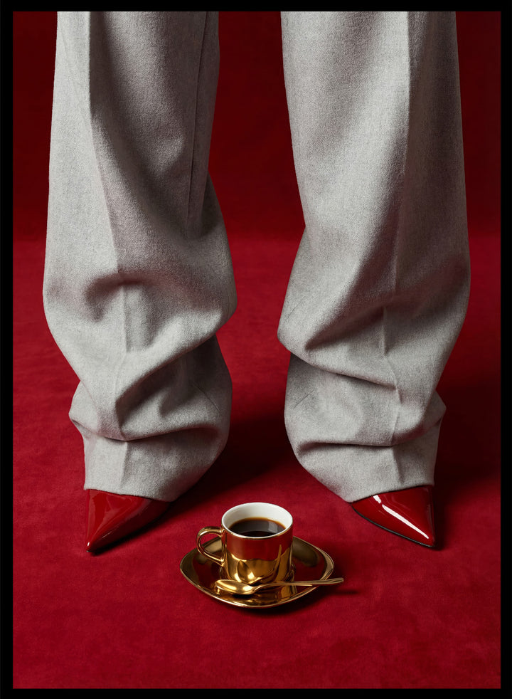 White pants with red shoes on a red carpet, featuring a gold cup and saucer with coffee. Red Shoes and Coffee by Andreas Magnusson is a fashion photography art print featuring red heels and espresso. Officially licensed modern wall poster.