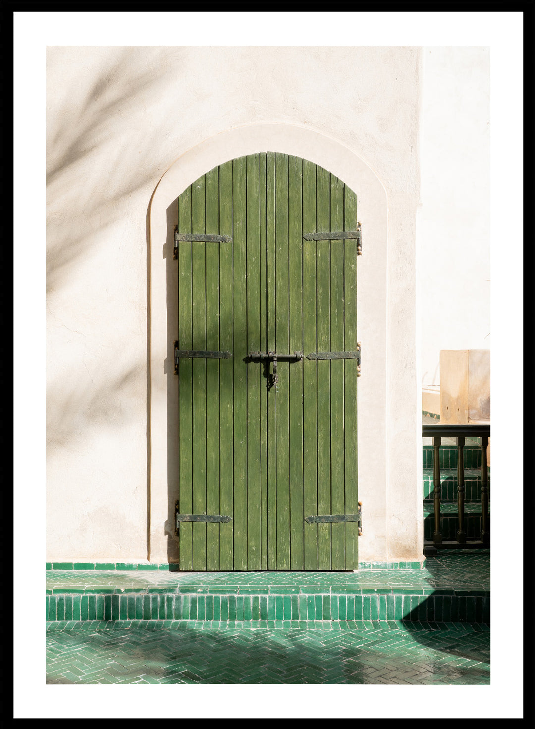 Green wooden door with metal latch on a white wall next to a pool. Moroccan Green Door by Henrike Schenk is an architectural photography print featuring green tilework, a traditional doorway, and Moroccan design details.