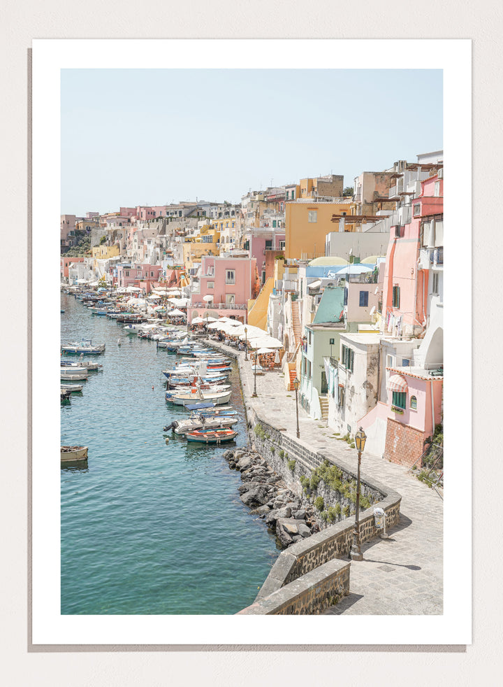 Colorful coastal town with boats docked along a waterfront. Colorful Italian Harbor by Henrike Schenk is a coastal photography print featuring pastel waterfront architecture, fishing boats, turquoise waters, and Mediterranean charm.