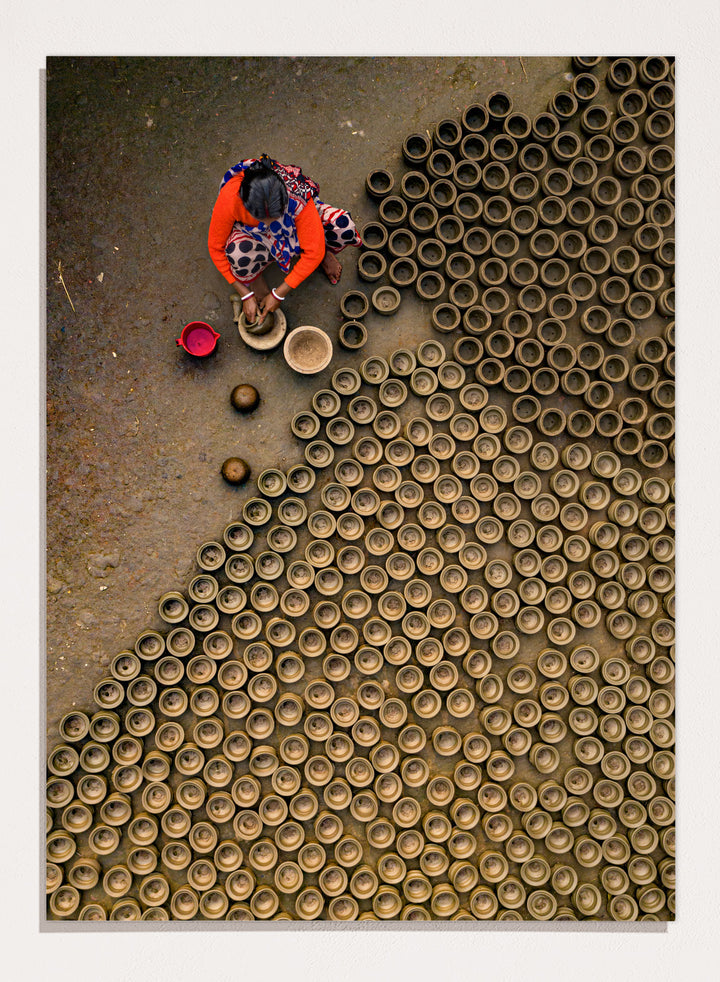 Person working with clay pots on a textured surface. Pot Making by Azim Khan Ronnie aerial photography print showing clay pots drying in Bangladesh village, traditional craft wall art poster
