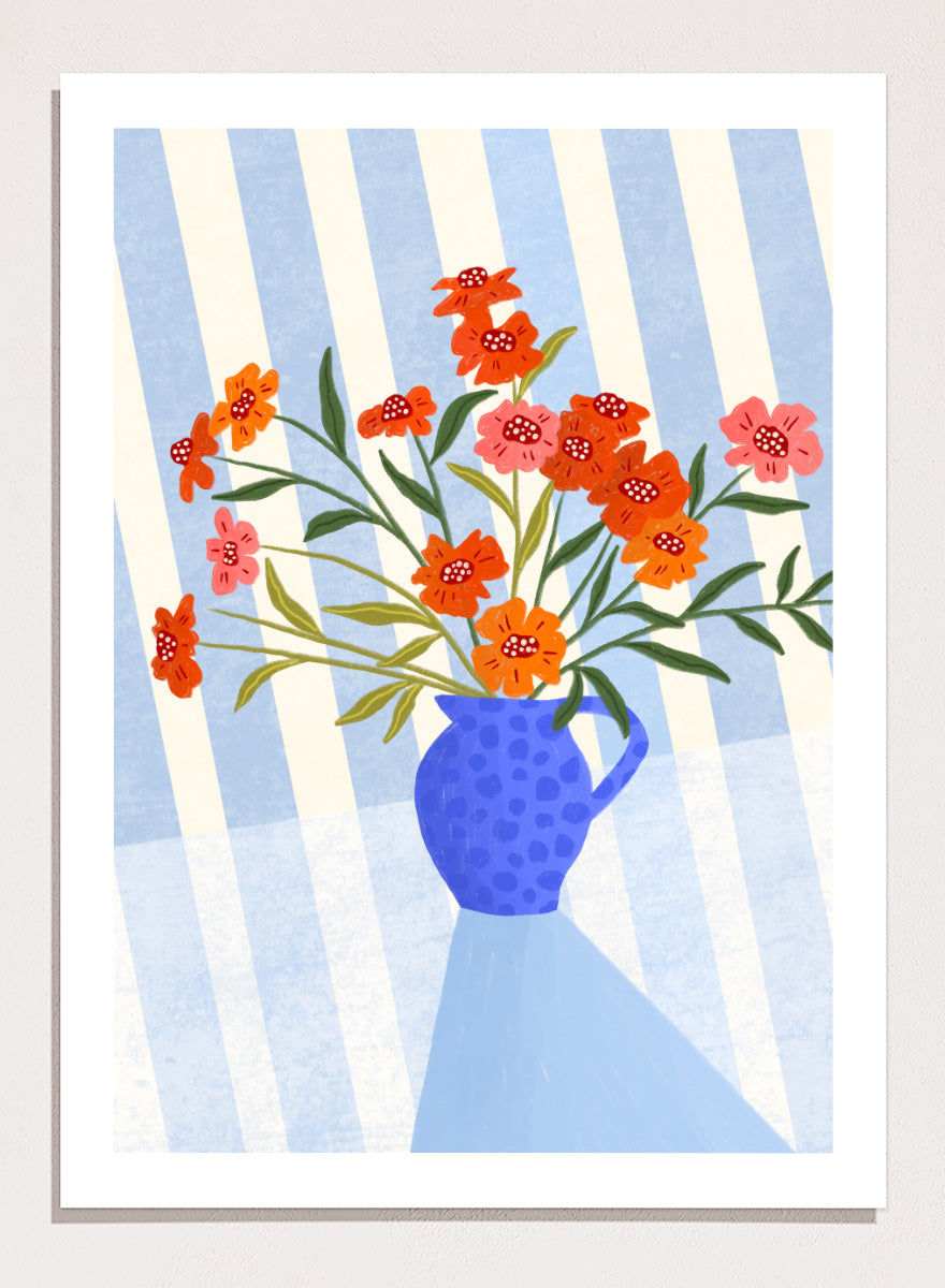 A framed art print featuring a stylized illustration of a blue patterned pitcher vase filled with orange, red, and pink flowers against a blue and white striped background. Cheerful Floral Pitcher by Bea Müller floral still life art print featuring orange and pink flowers in a bright blue jug with striped blue decor.