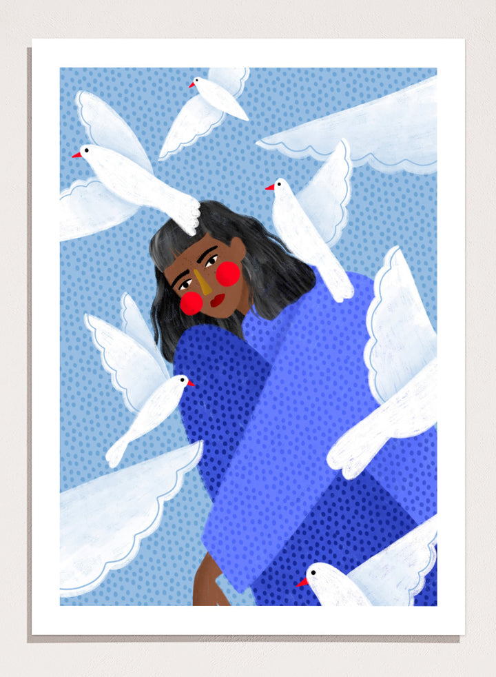 A framed art print featuring a stylized illustration of a woman with dark hair and red cheeks, wrapped in a blue patterned blanket, surrounded by white doves against a light blue dotted background. Peaceful Woman and Doves by Bea Müller art print featuring a woman in blue surrounded by white birds, layered textures, and soft modern color.