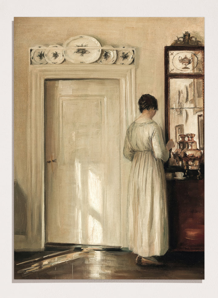 Woman in a white dress standing in a room with a door and shelves filled with items. Woman Making Tea by Carl Holsøe is a vintage Danish interior art print featuring Scandinavian home interiors, muted tones, natural light, and a woman preparing tea.