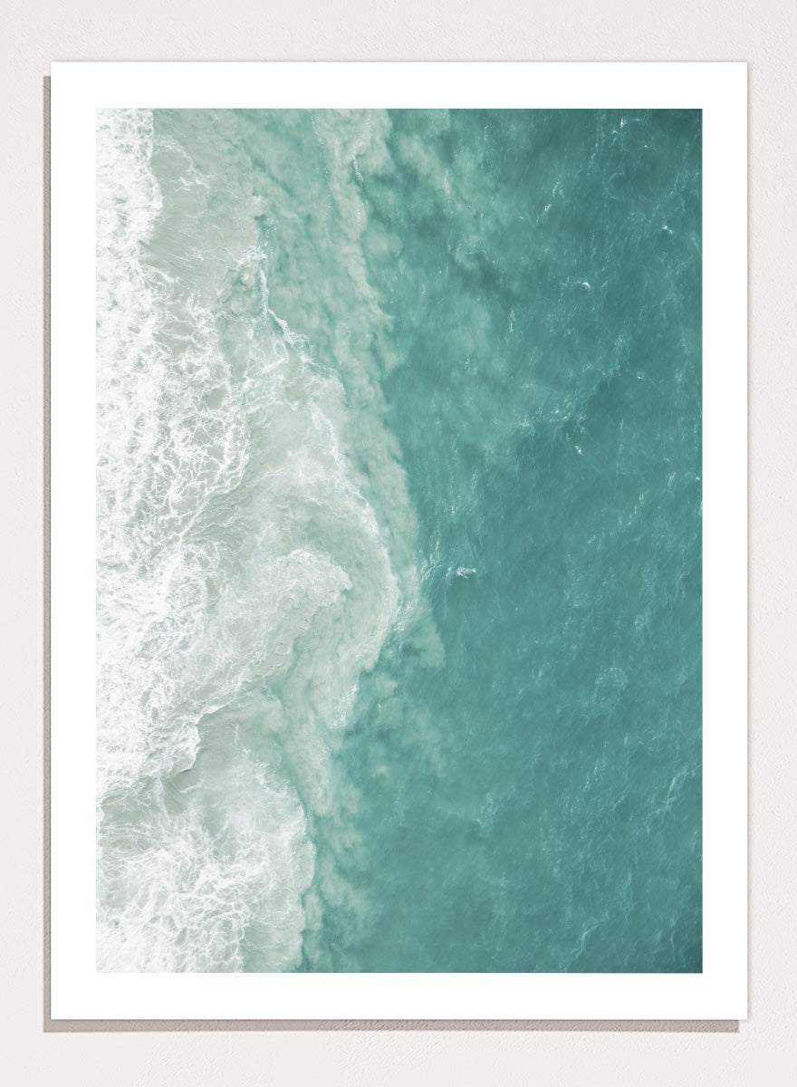 A framed aerial photograph of ocean waves, showing white foam breaking into turquoise and teal water. Ocean’s Edge by Shot by Clint aerial ocean photography print featuring turquoise water, white surf, and layered coastal movement.