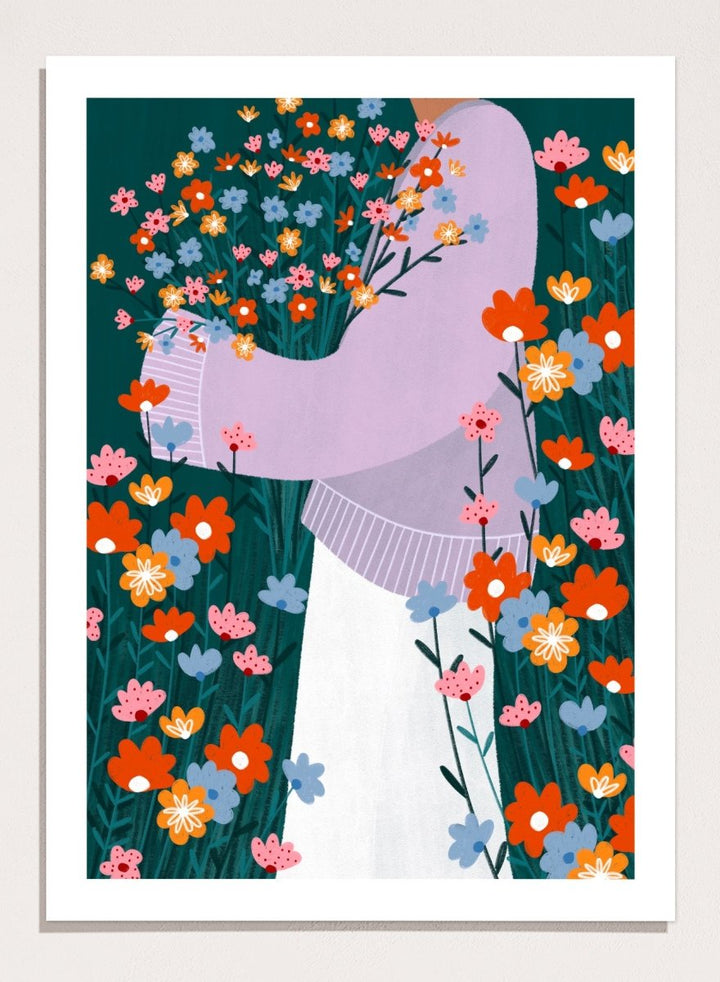 A stylized art print featuring a woman in a lavender sweater and white skirt holding a large bouquet of colorful wildflowers, framed by dense flowers on a dark teal background. Happy Woman Holding Flowers by Bea Müller premium framed fine art print featuring a woman carrying wildflowers in bright orange, pink, blue, and teal.