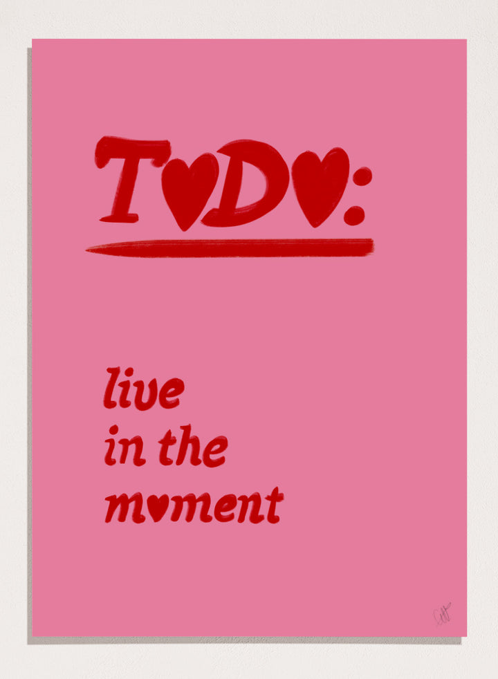 Pink poster with red text 'TODO: live in the moment' on a pink background. Typography wall art reading “live in the moment” with red hearts on pink background by Anne-Marie Volfova. Officially licensed motivational art print.