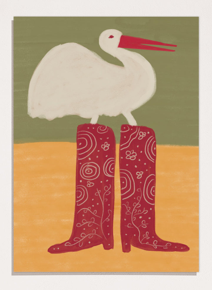A stylized art print featuring a white stork with a red beak standing on a pair of tall red boots with white swirl patterns, set against a muted green and ochre background. Bird in Red Boots by The Art Concept playful animal art print featuring a white bird in oversized red patterned boots with soft green and ochre tones.