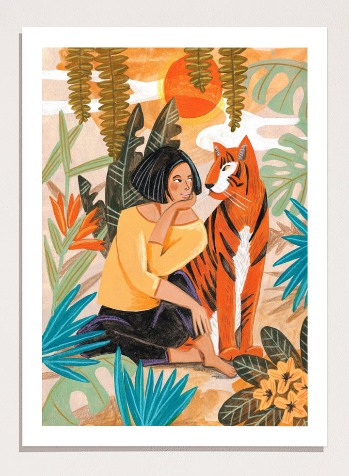 A framed art print featuring a stylized illustration of a woman in a yellow top and black skirt sitting beside an orange tiger, surrounded by tropical leaves and a warm orange sky. Woman with Tiger by Caroline Bonne Müller tropical art print featuring a woman beside a tiger among lush foliage, bold color, and hand-drawn texture.