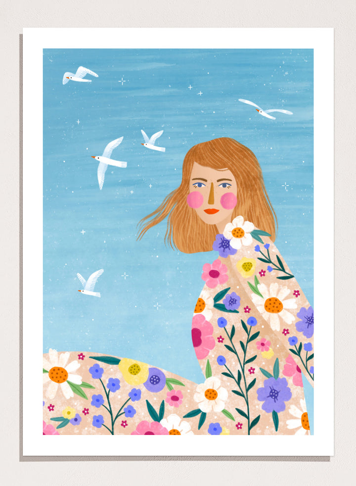 A framed art print featuring a stylized illustration of a young woman with long light brown hair, surrounded by colorful flowers and white birds against a light blue sky. ree Spirit Floral Dreams by Bea Müller floral woman art print featuring a flowing flower-covered summer dress, white birds, and a bright blue sky.