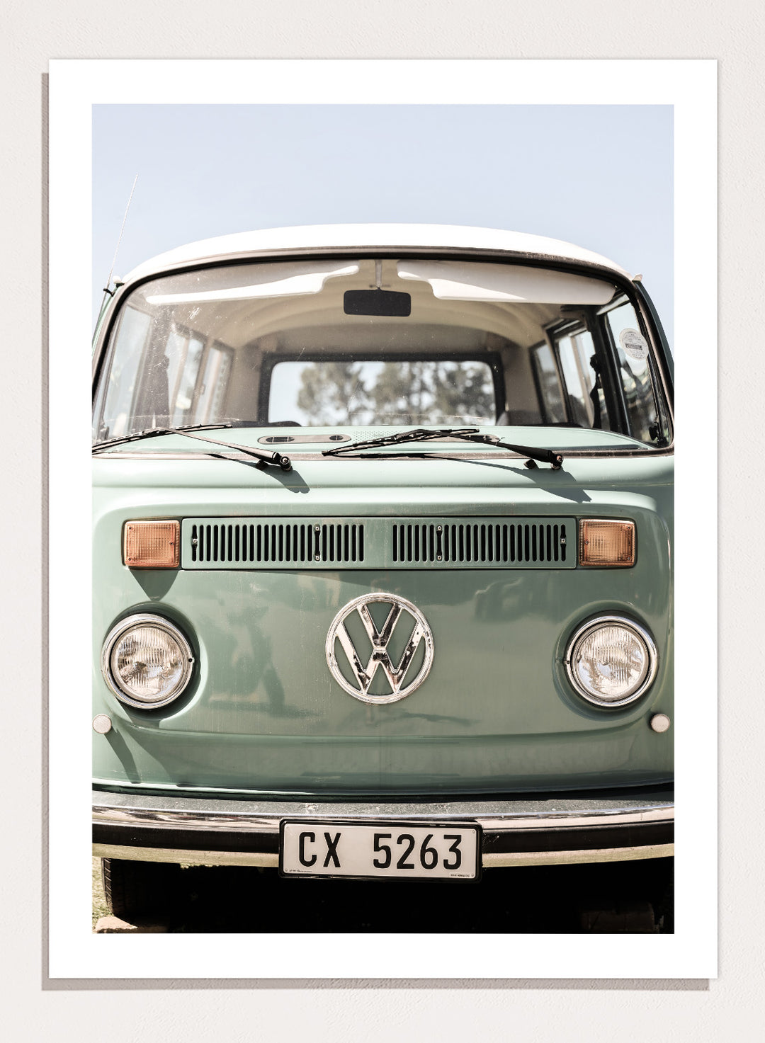 Front view of a vintage green Volkswagen van with clear sky background. Classic Design In Soft Green Tones by Shot by Clint car art print featuring a vintage Volkswagen camper van in soft sage green and warm sunlight.