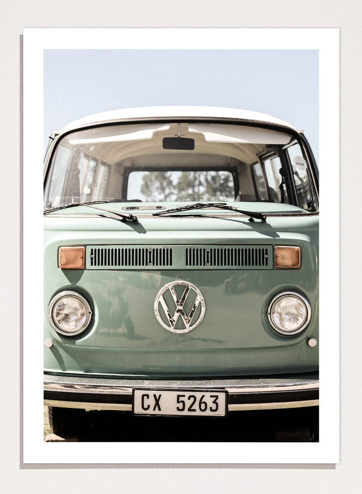 Front view of a vintage green Volkswagen van with clear sky background. Classic Design In Soft Green Tones by Shot by Clint car art print featuring a vintage Volkswagen camper van in soft sage green and warm sunlight.