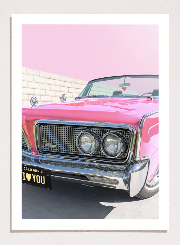 Pink vintage car with 'I ❤️ YOU' license plate against a pink sky. P.S. I Love You by Tom Windeknecht is officially licensed photography featuring a vibrant pop-art style photo of a car with romantic typography. Framed or unframed.