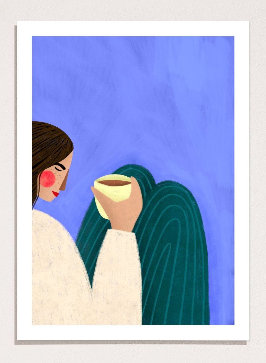A framed minimalist art print featuring a stylized woman in profile with brown hair, a cream sweater, and a dark teal cape against a textured blue background, holding a pale yellow cup. Peaceful Coffee Moment by Bea Müller premium framed fine art print featuring a woman curled up with a warm drink in soft blue, cream, and teal tones.