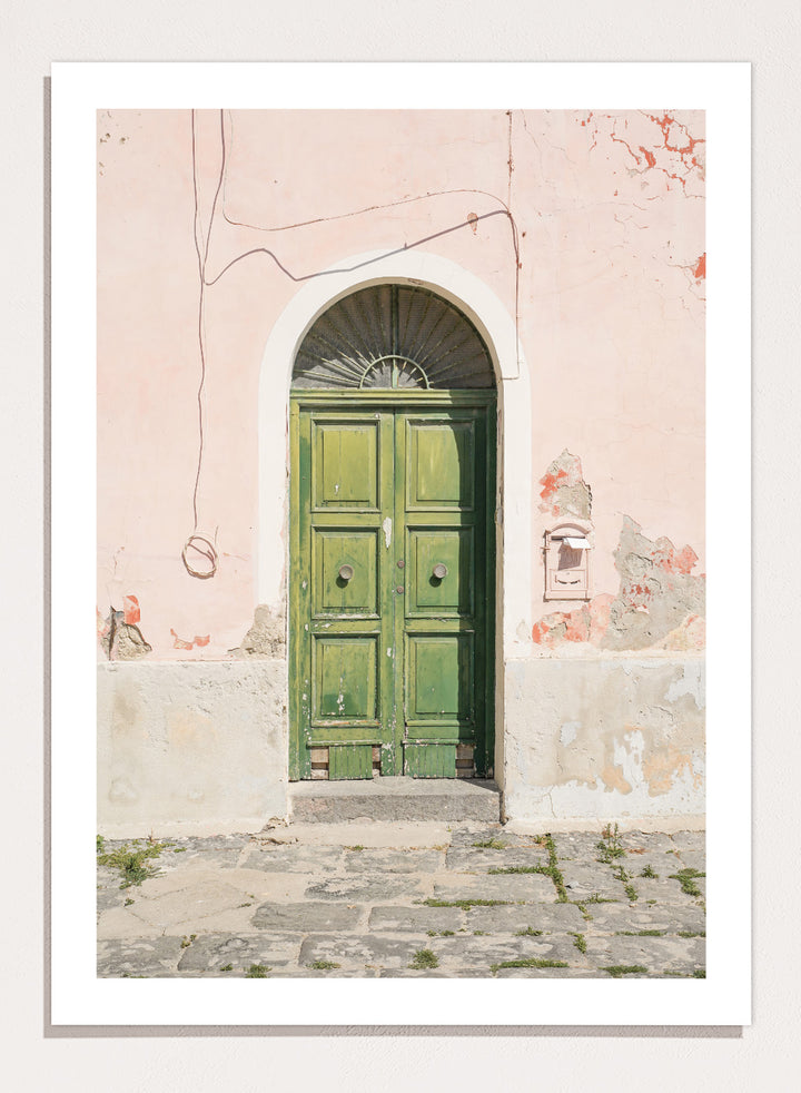 Green door on a pink wall with peeling paint. Old World Green Door by Henrike Schenk features a vintage European doorway, weathered architecture, pastel walls, travel photography, and wall art.
