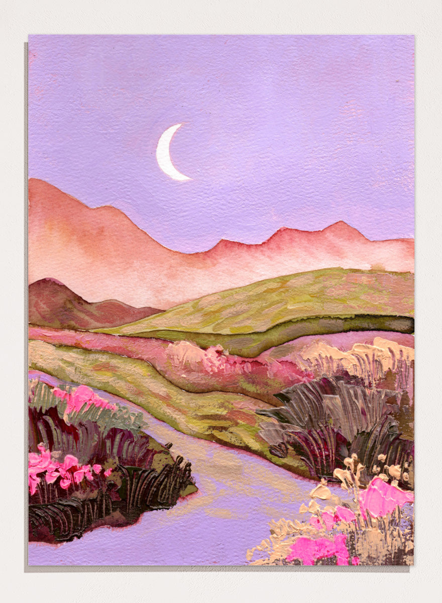 A landscape painting featuring rolling green hills, pink mountains, a purple sky with a crescent moon, and pink flowers along a winding path. Shop Moonlit Valley Path by Ekaterina Prisich, a colorful landscape art print featuring a crescent moon, winding path, rolling hills, and wildflowers.