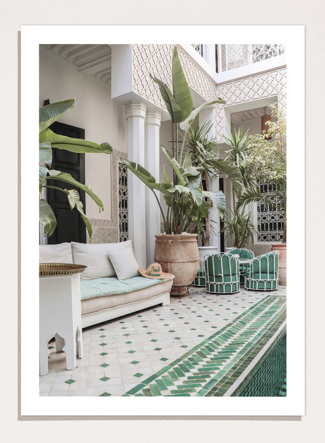 Outdoor patio with white sofa, green chairs, and potted plants in a decorative courtyard. Moroccan Riad Courtyard Oasis by Henrike Schenk is a Morocco photography print of a riad courtyard with tropical plants, tilework, and interior decor.