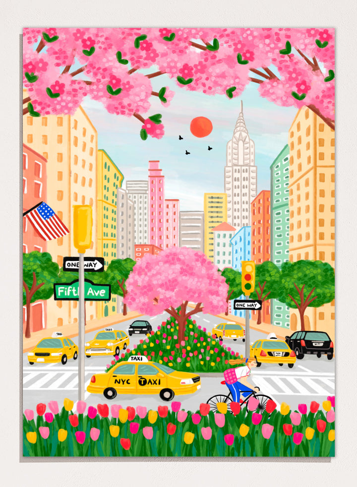 A colorful illustrated city street scene with pink cherry blossoms overhead, yellow NYC taxis, tall buildings, a bicycle with a pink basket, flowers in the foreground, and street signs including Fifti Ave. Shop NYC Cherry Blossoms by Nidhi Kachhadiya, a colorful New York City wall art print with Fifth Avenue, yellow taxis, pink blossoms, and spring city charm.