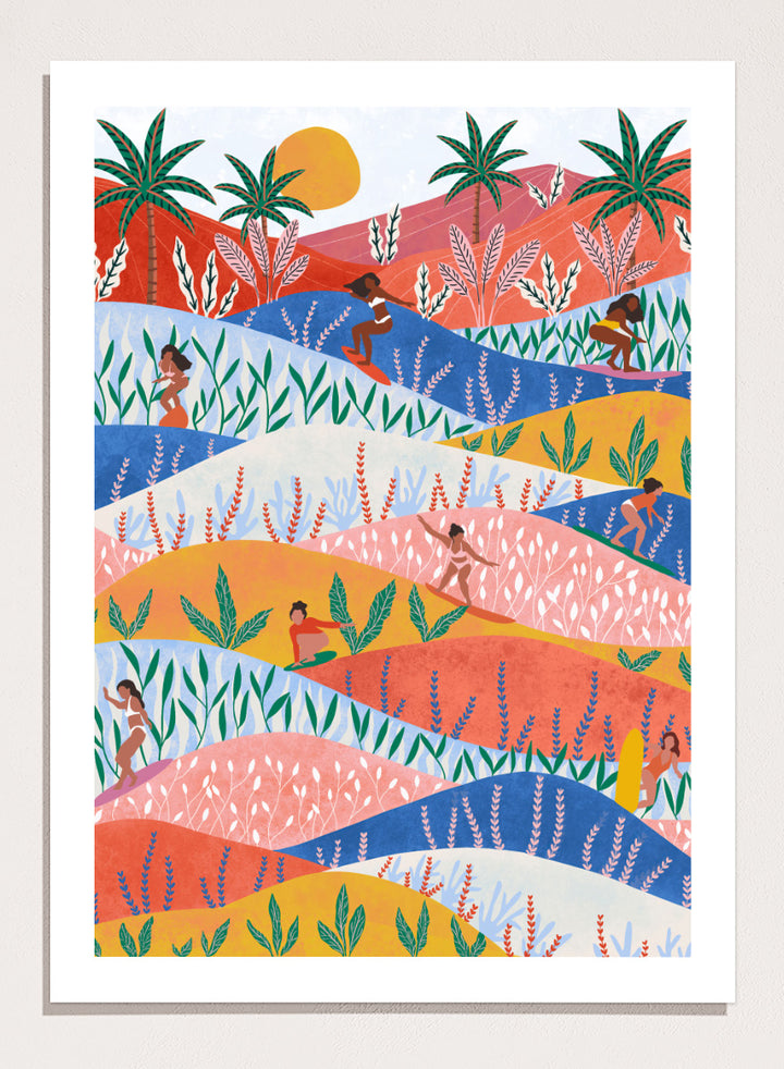 A framed art print featuring a colorful, stylized landscape illustration with rolling hills, palm trees, a sun, and small human figures in a folk-art style. Tropical Surf Girls by Ceyda Alasar surf art print featuring women riding waves through a colorful palm-filled landscape in bold tropical tones.