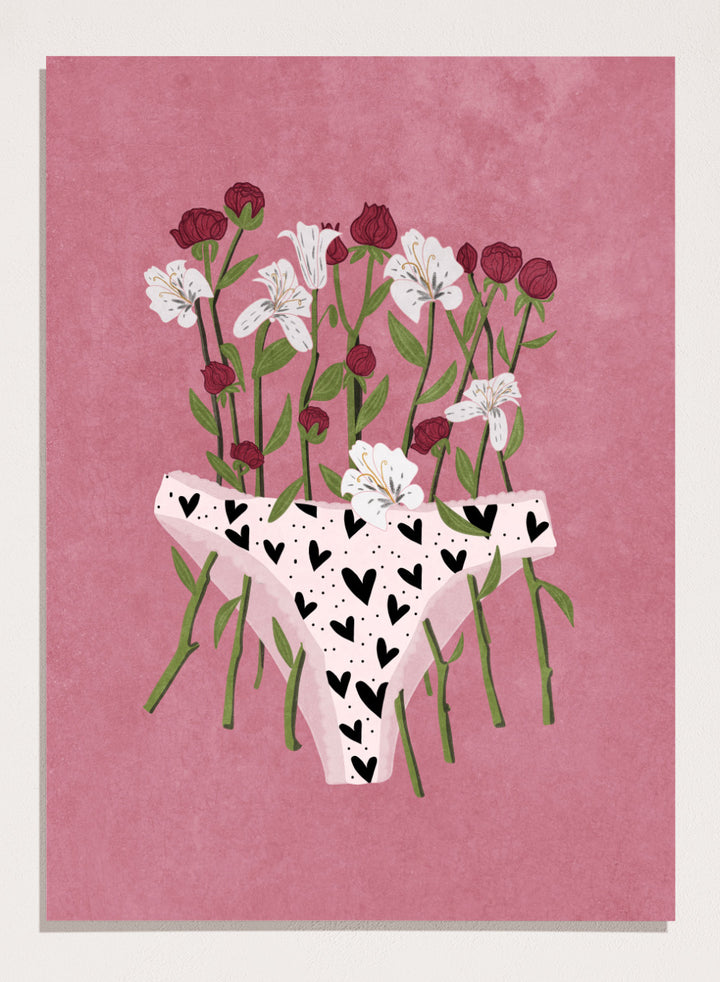 White underwear with black heart patterns surrounded by flowers on a pink background. Blooming Slip by Raissa Oltmanns features a feminist illustration of flowers growing from heart-patterned underwear on a pink background. Bold floral art print with strong feminine symbolism.