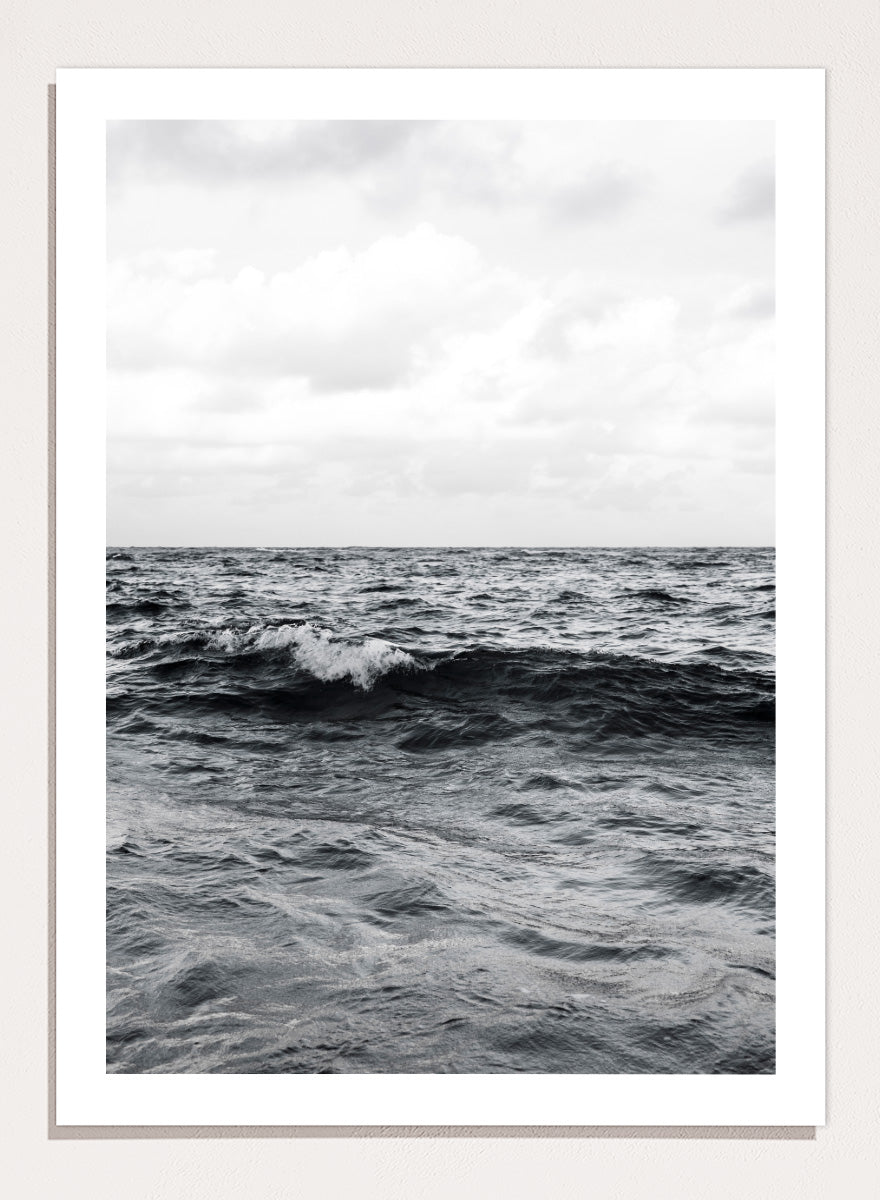 Black and white photographic art print of ocean waves under a cloudy sky. Endless Waves by Shot by Clint black-and-white ocean photography print featuring rolling water, textured surf, cloudy skies, and dramatic coastal movement.
