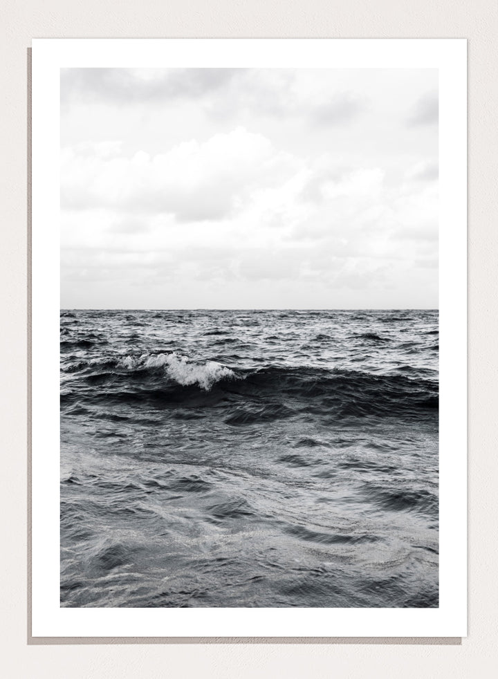 Black and white photographic art print of ocean waves under a cloudy sky. Endless Waves by Shot by Clint black-and-white ocean photography print featuring rolling water, textured surf, cloudy skies, and dramatic coastal movement.