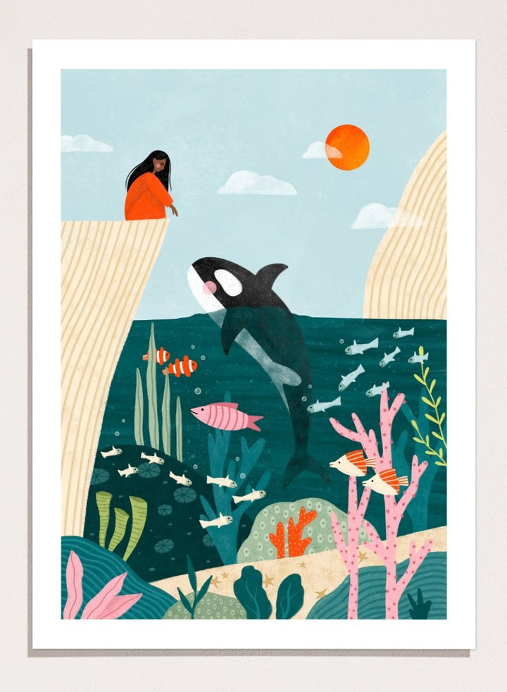 A framed art print featuring a whimsical underwater scene with an orca, coral, fish, and a woman in an orange dress standing on a cliff edge under a sun. Girl Watches Ocean Life by Bea Müller premium framed fine art print featuring a child watching an orca swim through a colorful underwater world.