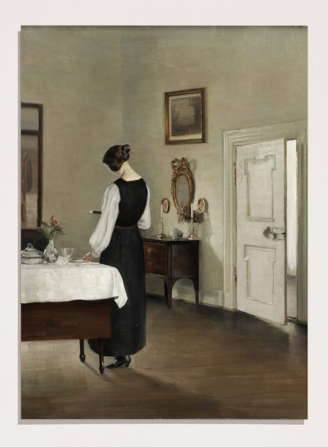Woman in a black dress standing in a room with a table and mirror. In the Dining Room by Carl Holsøe is a vintage Danish interior art print featuring a woman in a softly lit dining room with muted tones and classic Scandinavian style.
