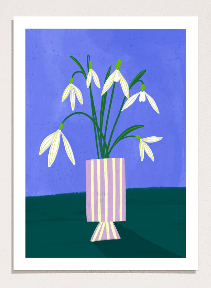 A framed art print featuring a stylized illustration of white snowdrops with green stems in a lavender and cream striped vase, set against a blue and dark green background. Snowdrops in Striped Vase by Bea Müller fine art print featuring white snowdrops, a lilac striped vase, and a deep blue background.
