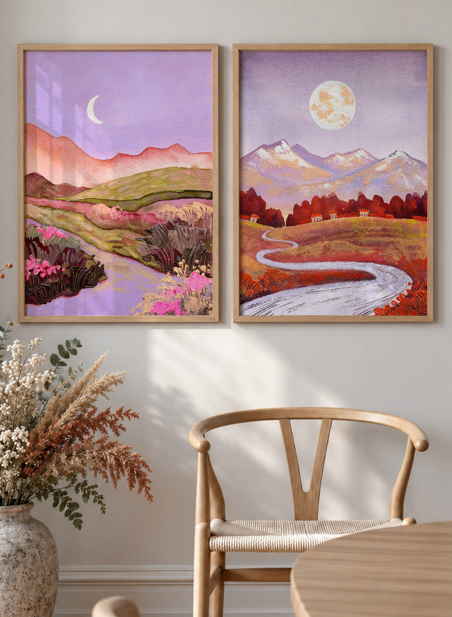 Two framed landscape art prints displayed side by side on a black shelf against a light beige wall. The left print shows a purple-toned valley with a crescent moon, pink flowers, and distant hills. Shop Moonlit Landscapes by Ekaterina Prisich, a set of 2 landscape wall art prints posters featuring moonlit mountains, winding paths, and purple tones.