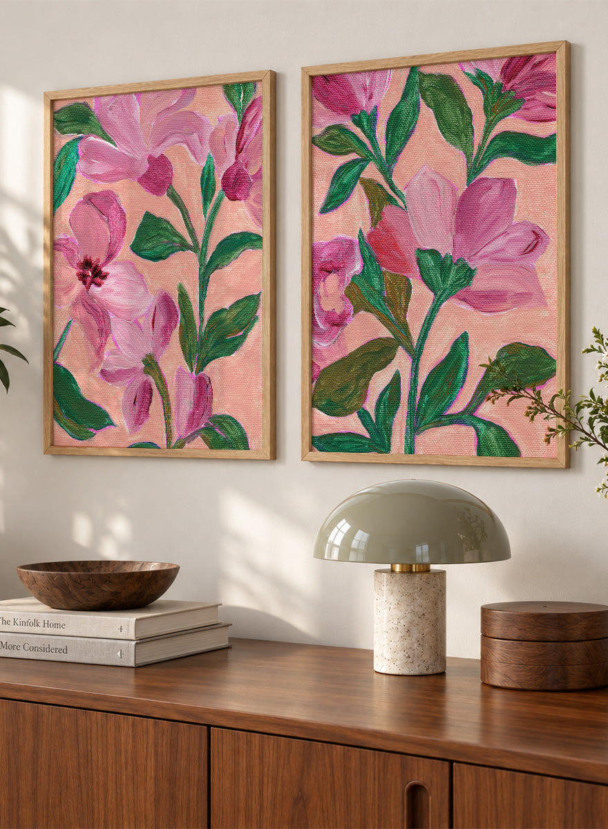 Two framed floral art prints with pink flowers and green leaves on a peach background. Shop Vibrant Pink Botanicals by Nikita Jariwala, a set of 2 floral wall art prints posters featuring oversized pink flowers and lush botanical artwork.