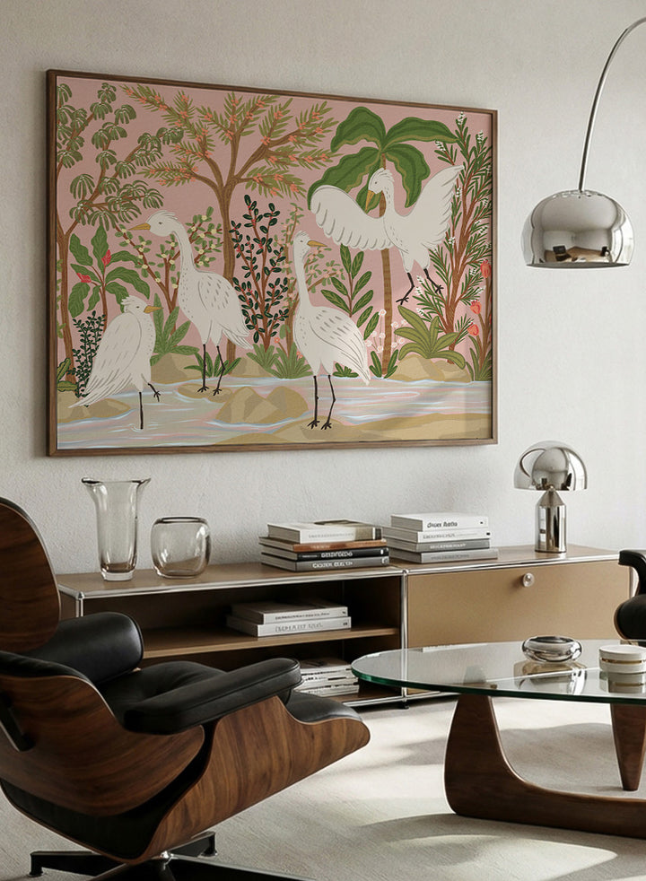 A framed art print featuring a stylized illustration of four white cranes in a tropical landscape with palm trees, green foliage, and a pink sky, displayed on a light beige wall. Shop Peaceful Jungle Egrets by Nikita Jariwala, a tropical bird wall art print featuring white egrets, lush greenery, botanical detail, and soft pink tones.a