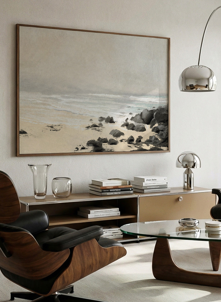 A framed beach landscape art print featuring a sandy shore, gentle waves, and dark rocks under a misty sky. Shop Beach by Dan Hobday, a contemporary coastal wall art print featuring sandy shoreline, ocean waves, dark rocks, soft blue-green water, and beige tones.