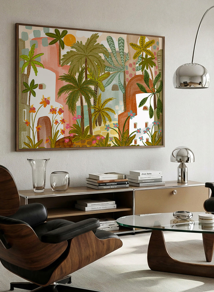 A framed art print featuring a whimsical, retro-style illustration of a tropical city with palm trees, colorful buildings, and flowers. Shop Vibrant Tropical Village by Nikita Jariwala, a tropical wall art print poster with palm trees, colorful village architecture, botanical scenery, and green tones.