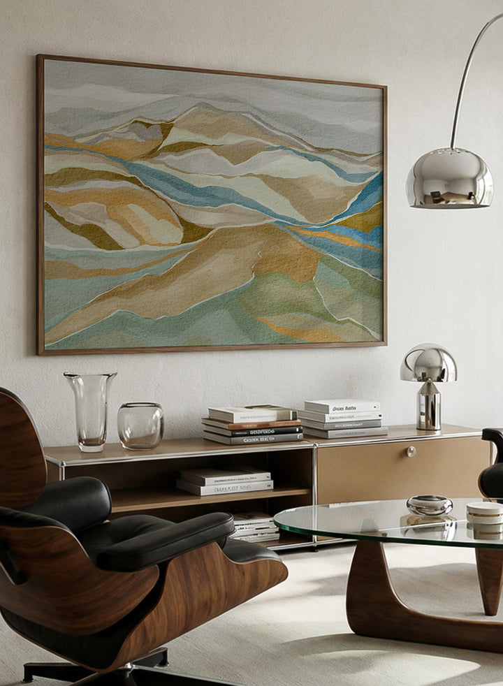 Framed abstract landscape wall art featuring layered hills and winding blue river-like lines in beige, tan, muted green, and blue tones, shown against a light neutral background. Shop Abstract Mountain Serenity by Nikita Jariwala, a modern mountain wall art print featuring layered abstract hills, earthy tones, and soft blue and sage accents.