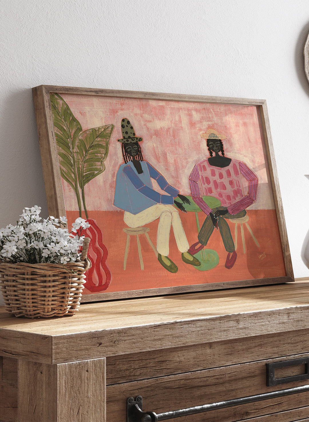 Artistic depiction of two people sitting on chairs with a plant and vase in the foreground, on a pink background. With a Friend by Studio IMO (Ibi Meier-Oruitemeka) is a modern figurative art print with two figures at a table in a contemporary wall poster design.