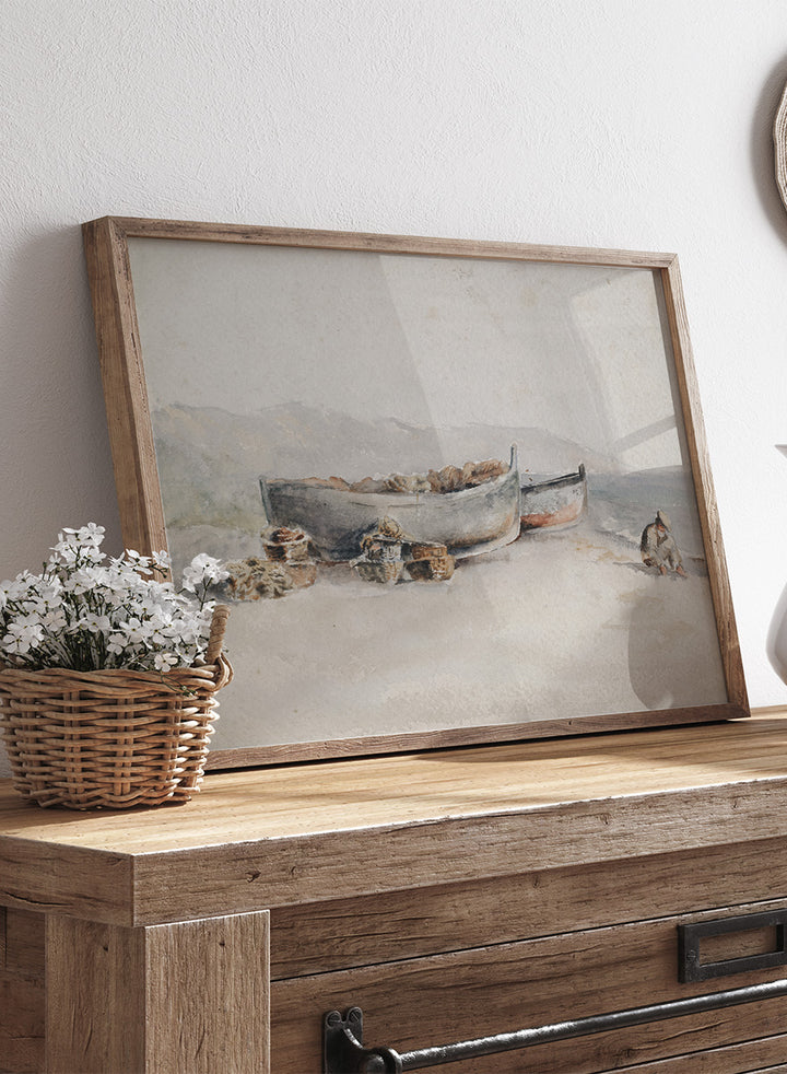 A framed watercolor painting depicting two boats on a sandy shore with rocks and a small seated figure. Fishing Boats on the Shore by Hercules Brabazon Brabazon is a vintage watercolor art print featuring fishing boats, nets, baskets, and a hazy coastal shore.