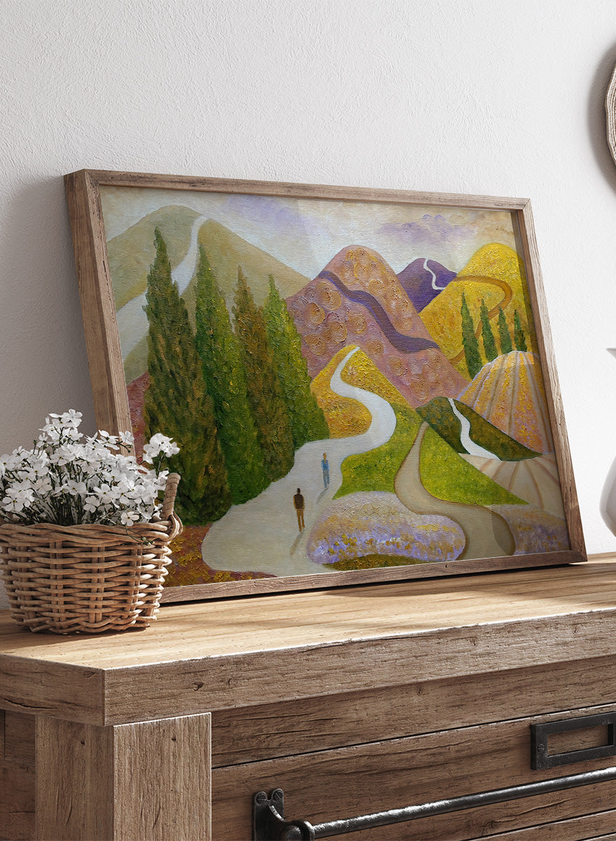 A framed landscape painting featuring stylized mountains, evergreen trees, winding paths, and small human figures, shown against a light neutral background. Shop Peaceful Journey Through Hills by Angeles M. Pomata, an autumn landscape art print featuring winding roads, cypress trees, rolling hills, and two walking figures.