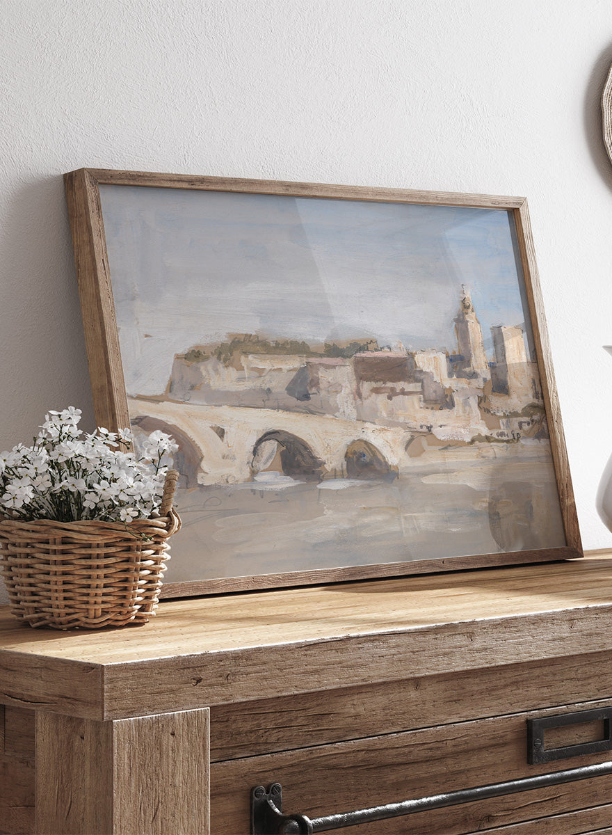 A framed art print depicting a scenic landscape with a stone bridge over water, historic buildings, and a church tower under a pale sky. Avignon; Bridge over a River by Hercules Brabazon Brabazon is a vintage watercolor art print featuring a stone bridge, river, and pale city skyline.