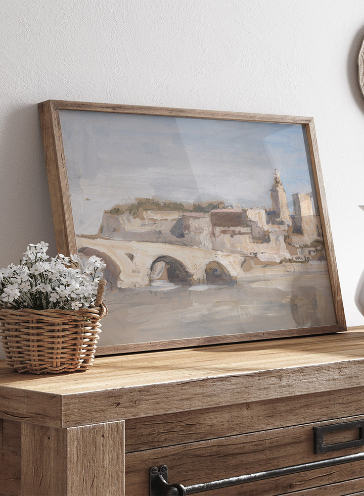 A framed art print depicting a scenic landscape with a stone bridge over water, historic buildings, and a church tower under a pale sky. Avignon; Bridge over a River by Hercules Brabazon Brabazon is a vintage watercolor art print featuring a stone bridge, river, and pale city skyline.