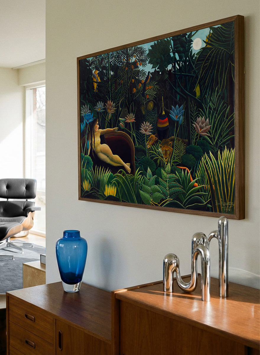 A framed art print depicting a lush, surreal jungle scene with a reclining nude woman in a boat, colorful flowers, birds, and animals under a full moon. The Dream by Henri Rousseau is a vintage jungle art print featuring a reclining woman, lush tropical plants, lions, flowers, and a moonlit forest.